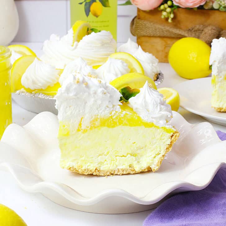 Lemon pie with whipped cream and lemon slices on a white serving dish.