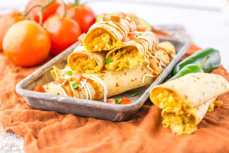 tray of Baked Cheesy Chicken Taquitos ready to serve, side tomatoes