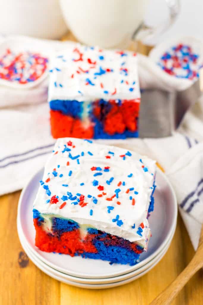 2 slices of red white and blue poke cake on white plates