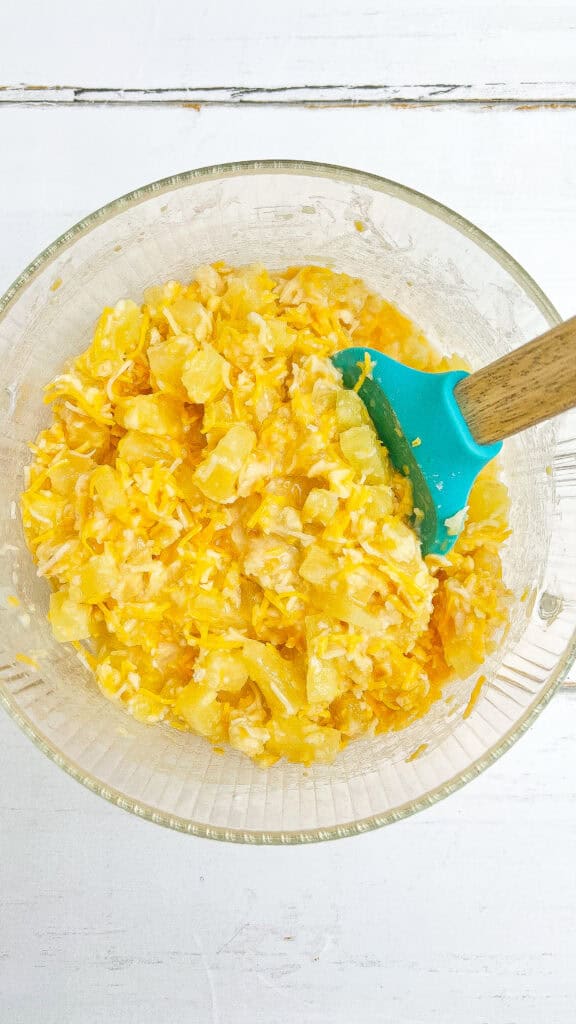 A bowl of ingredients for pineapple casserole mixed blue spatula.