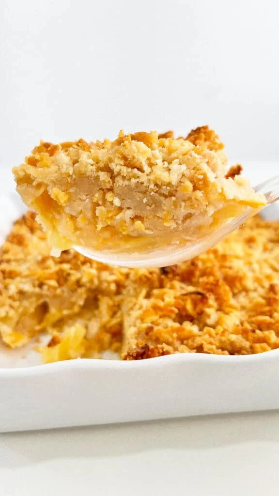 A spoon lifting a piece of pineapple casserole from a white dish.