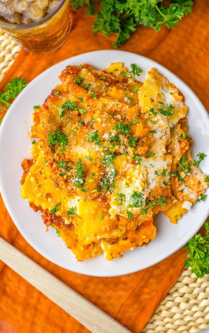 Creamy baked lasagna with melted cheese and fresh parsley on a white plate.