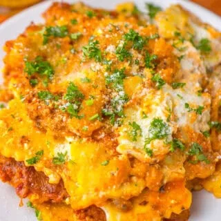 Cheesy meat lasagna with fresh herbs on a white plate.