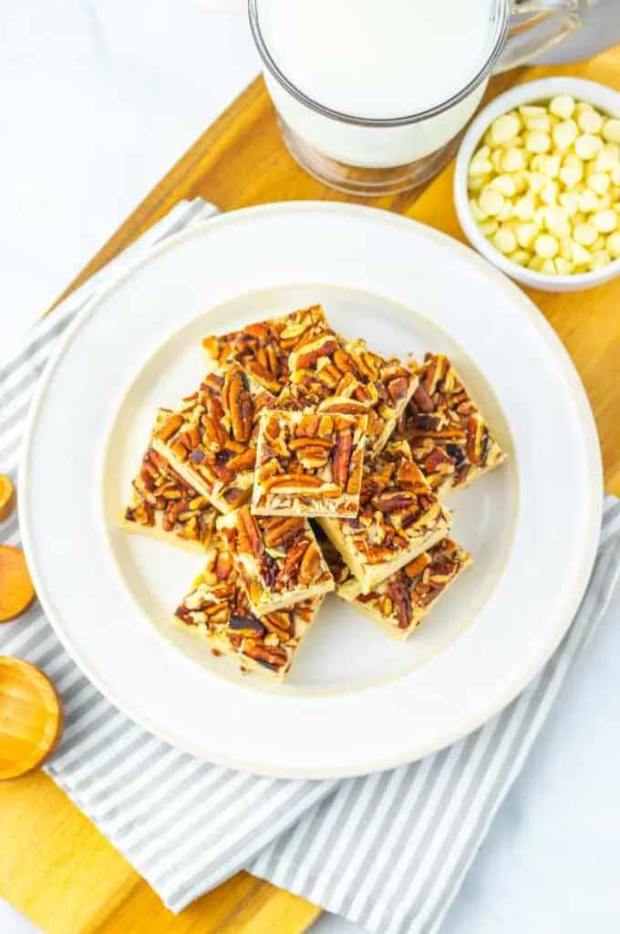 Golden Pecan pie fudge on a white plate with milk and white chocolate chips around.