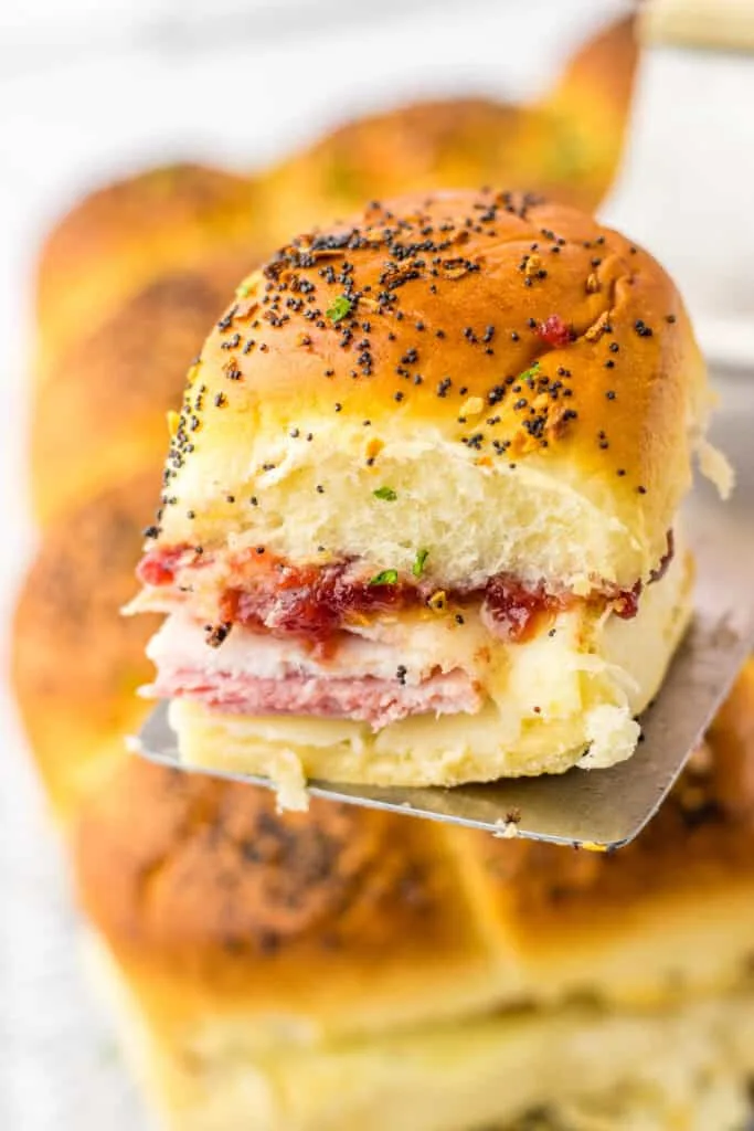 Golden baked roll with ham, turkey, cheese, and savory seasoning, on a metal spatula.