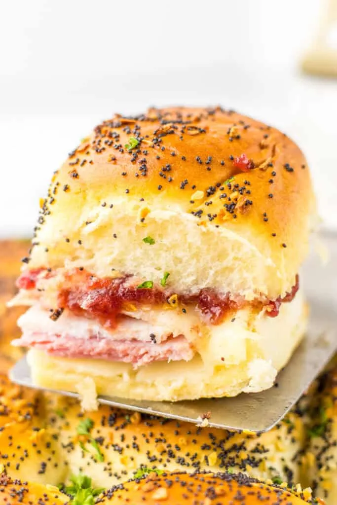 Cranberry Club Slider with ham, cheese, and tomato, topped with black pepper and herbs.