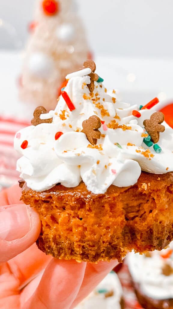 Gingerbread Cheesecake Bites cupcake with whipped frosting, colorful sprinkles, and holiday themed decorations.