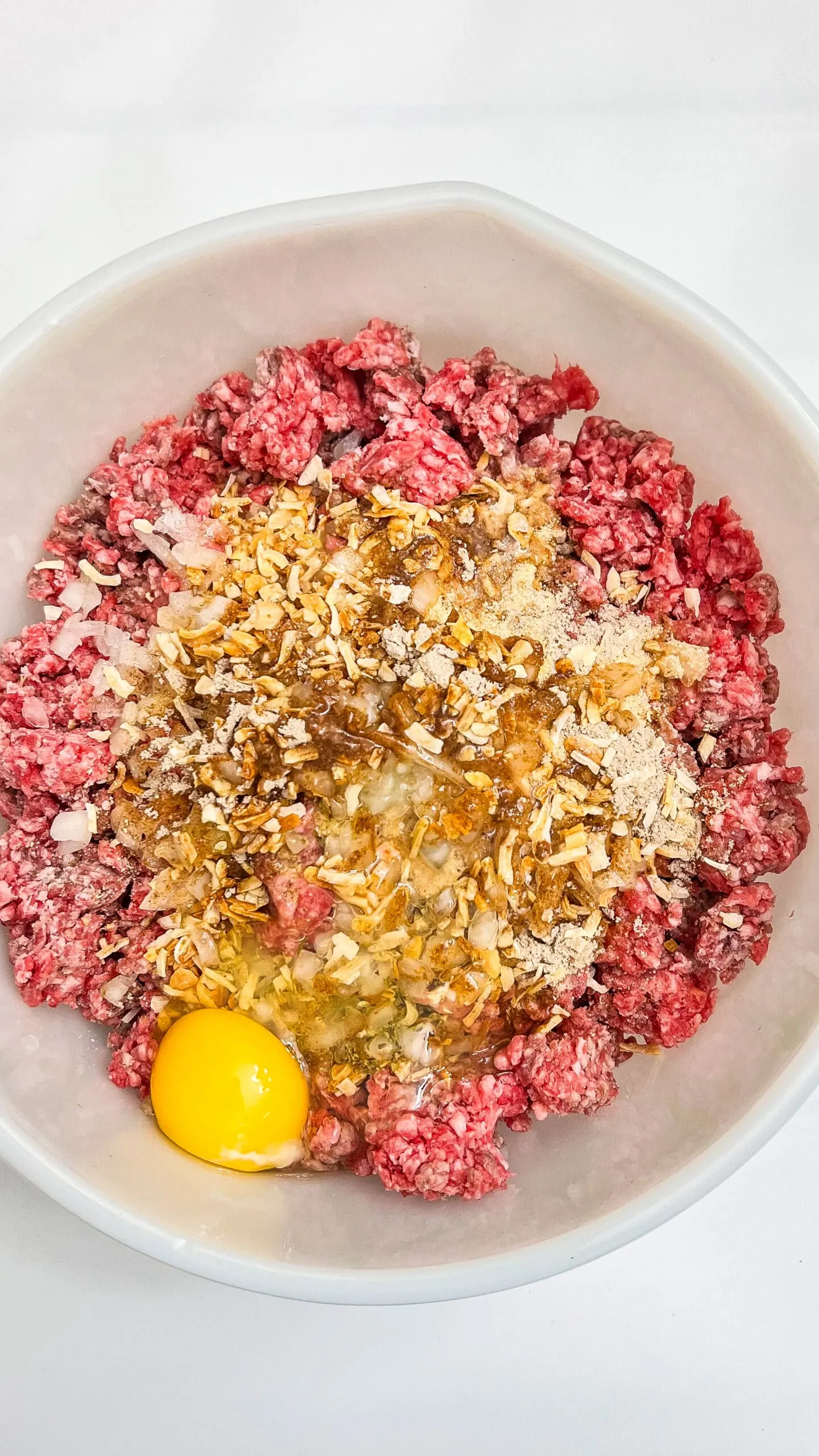 Juicy ground beef with eggs, bread crumbs, and chopped onions for homemade meatloaf preparation.