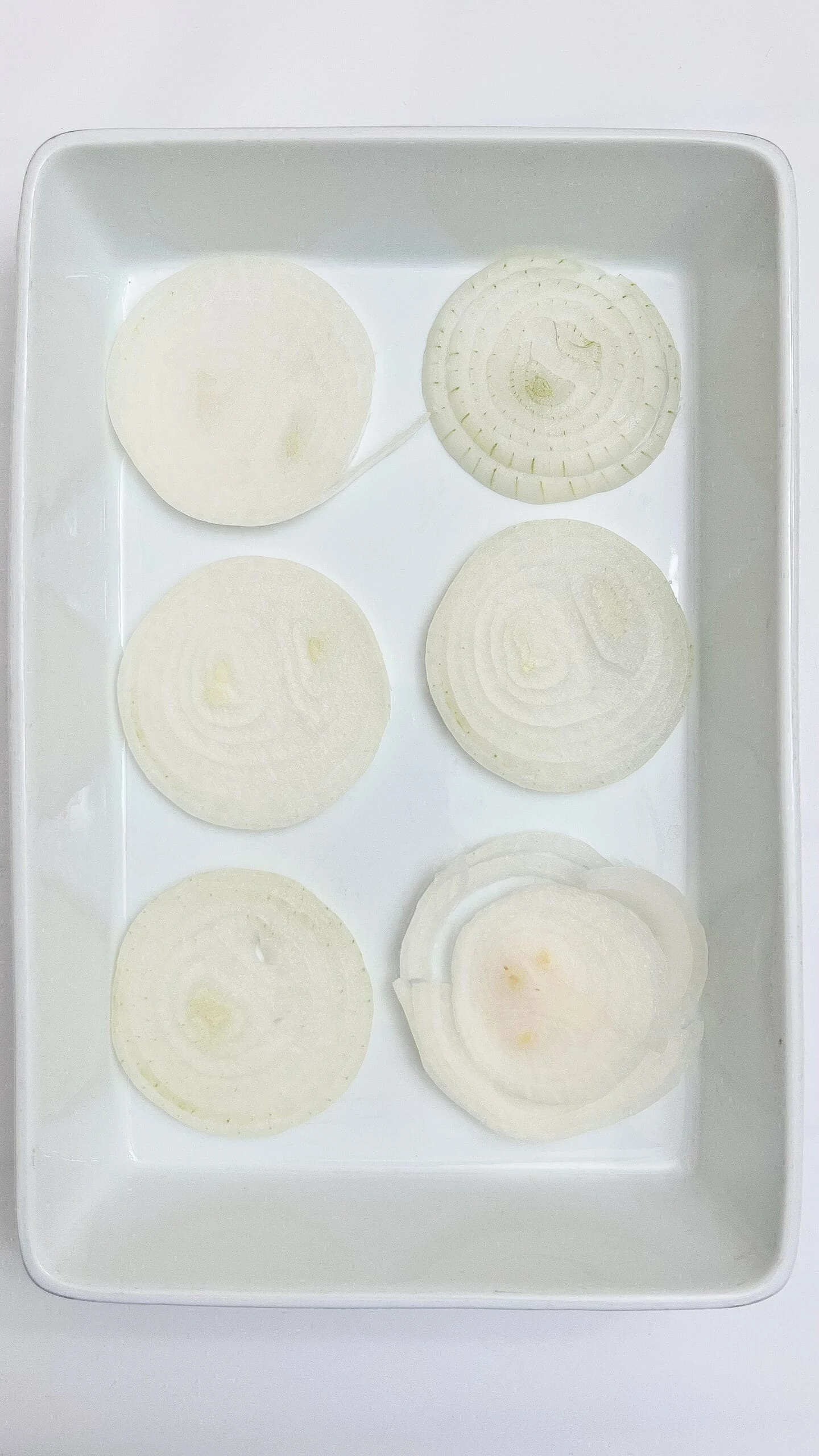 Thinly sliced onions arranged neatly on a white tray for chopping or cooking.