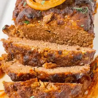 Alt text: Juicy meatloaf topped with caramelized onions and fresh herbs, served over spice-roasted cabbage.