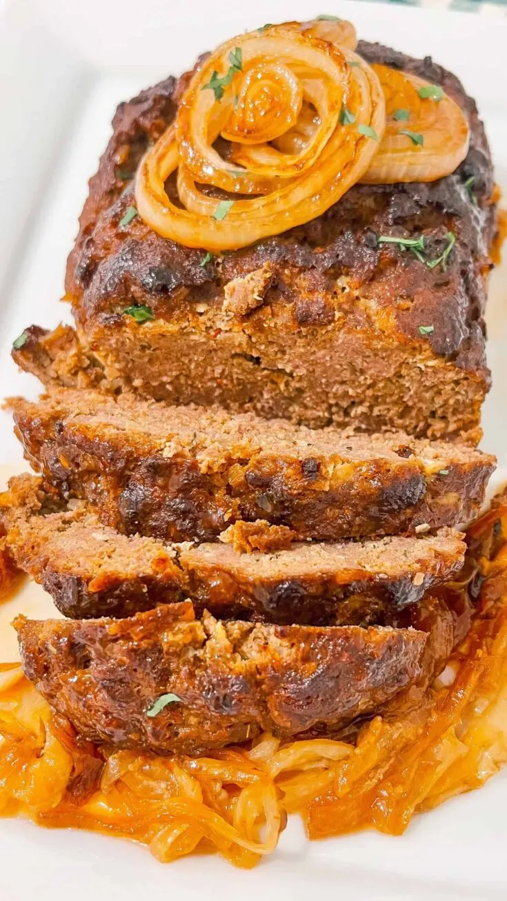 Alt text: Juicy meatloaf topped with caramelized onions and fresh herbs, served over spice-roasted cabbage.