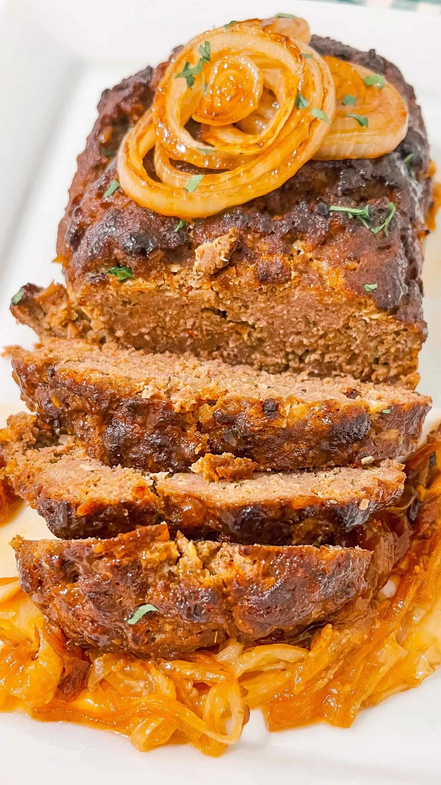 Alt text: Juicy meatloaf topped with caramelized onions and fresh herbs, served over spice-roasted cabbage.