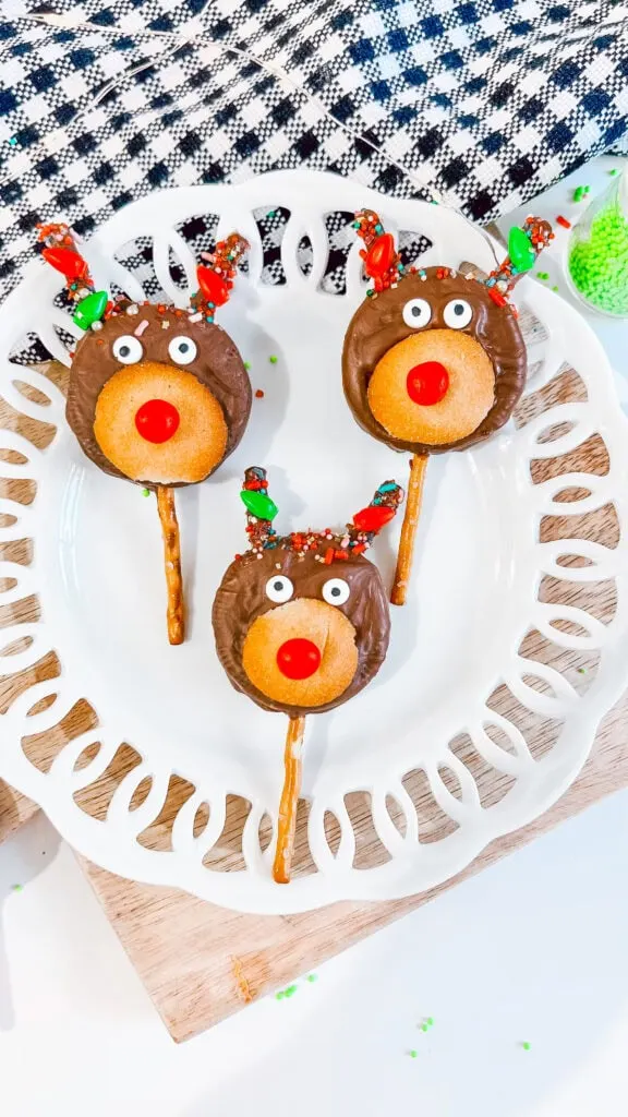 Adorable reindeer shaped cookies with chocolate coating, red nose, and candy eyes, perfect for holiday desserts.reindeer oreo pops on white platter