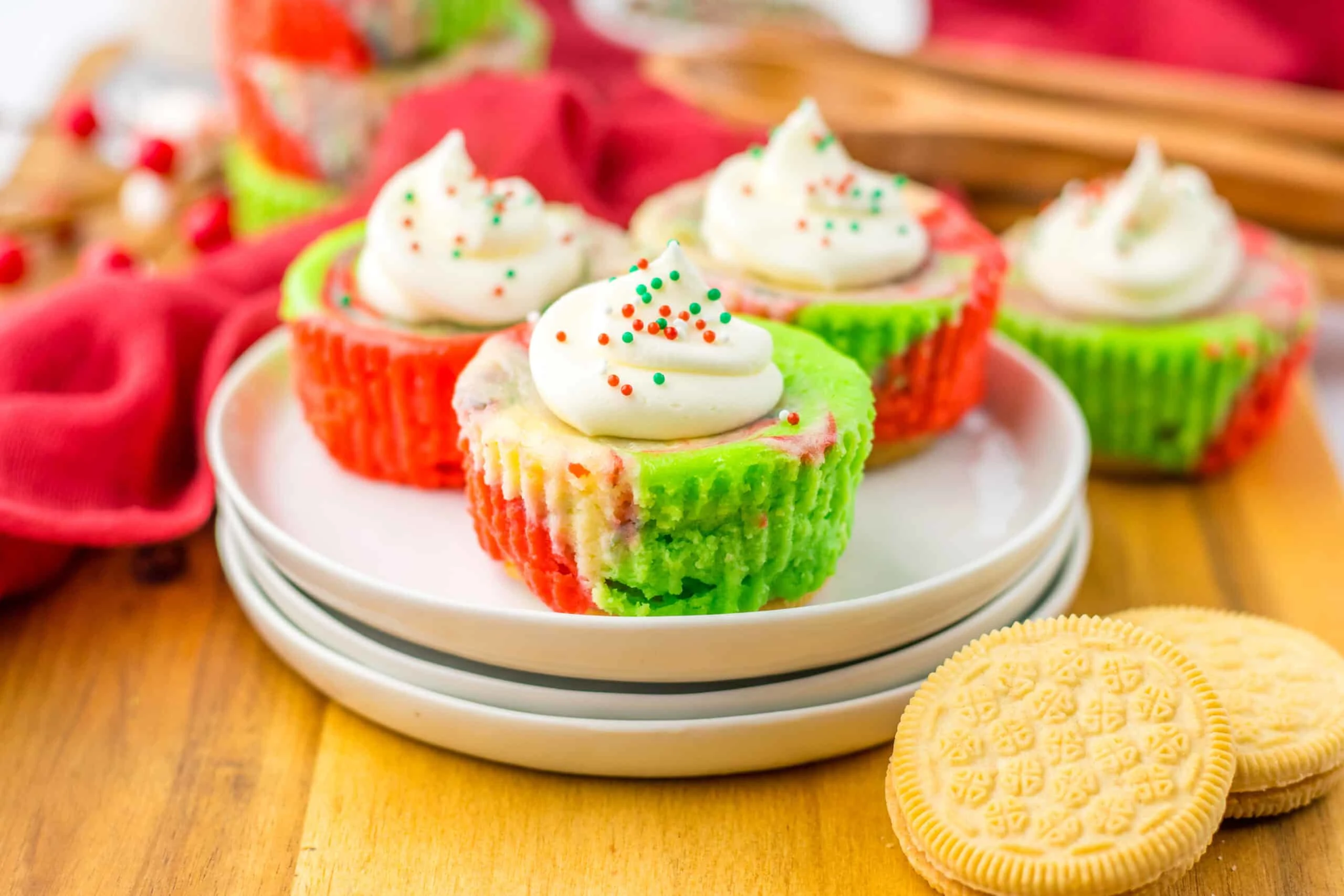 Festive cupcakes with green and red swirled liners, topped with whipped cream and holiday sprinkles, perfect for Christmas.