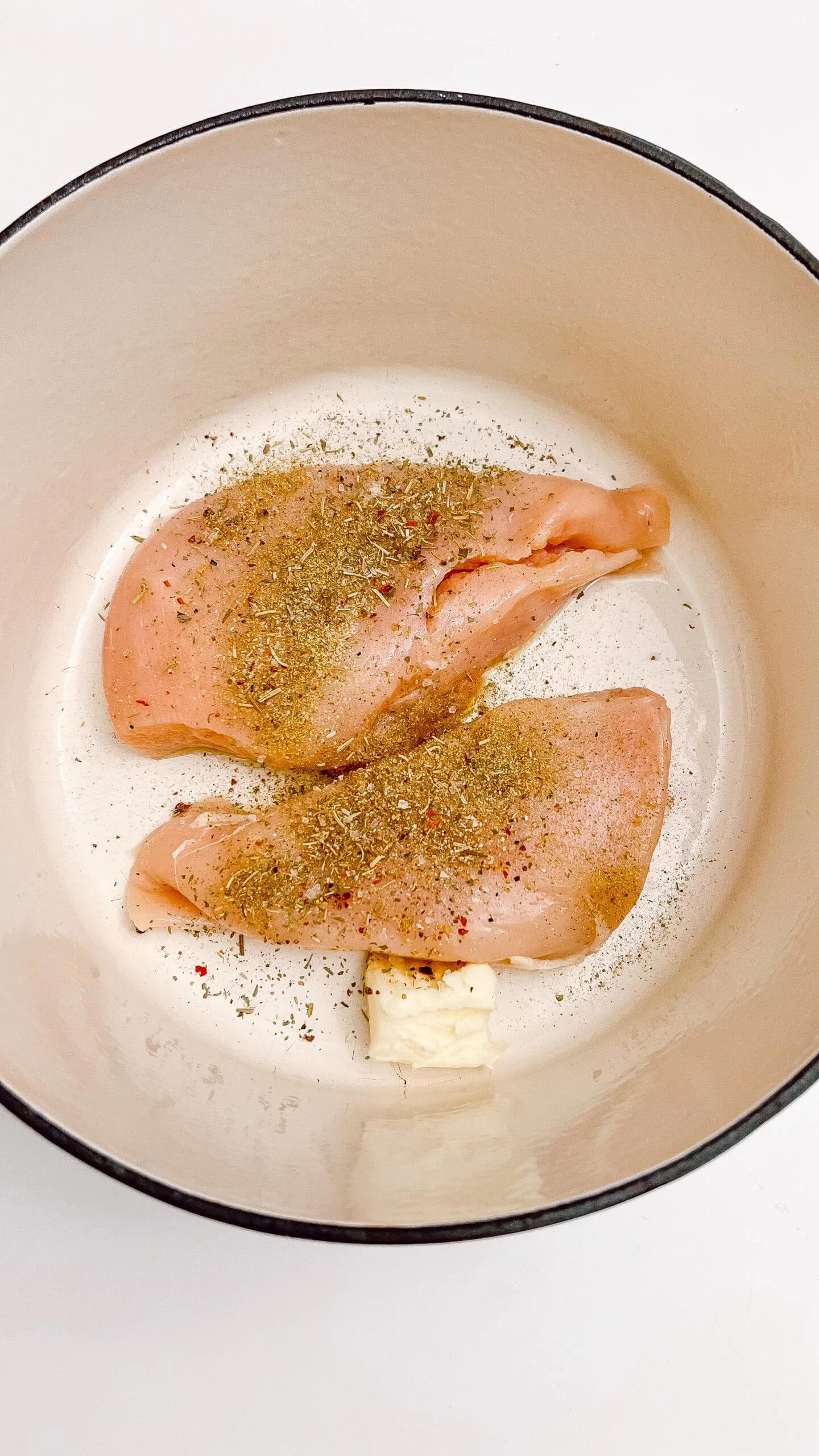 Raw chicken breasts seasoned with herbs and spices in a cooking pan.