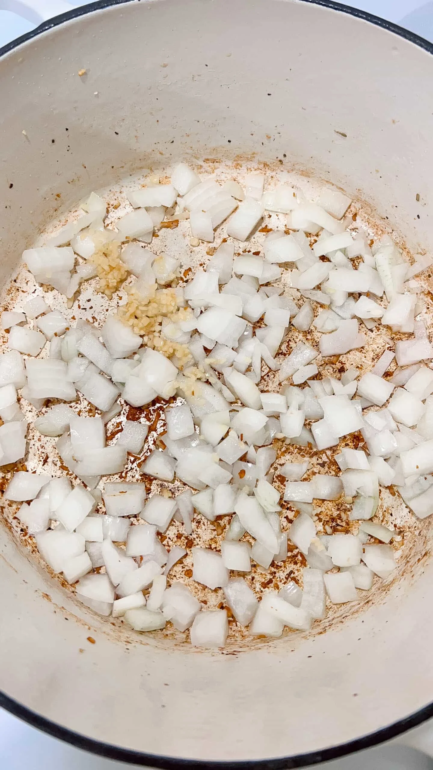 A close-up of diced onions and minced garlic saut&eacute;ing in a cast iron skillet, creating a savory base for cooking.