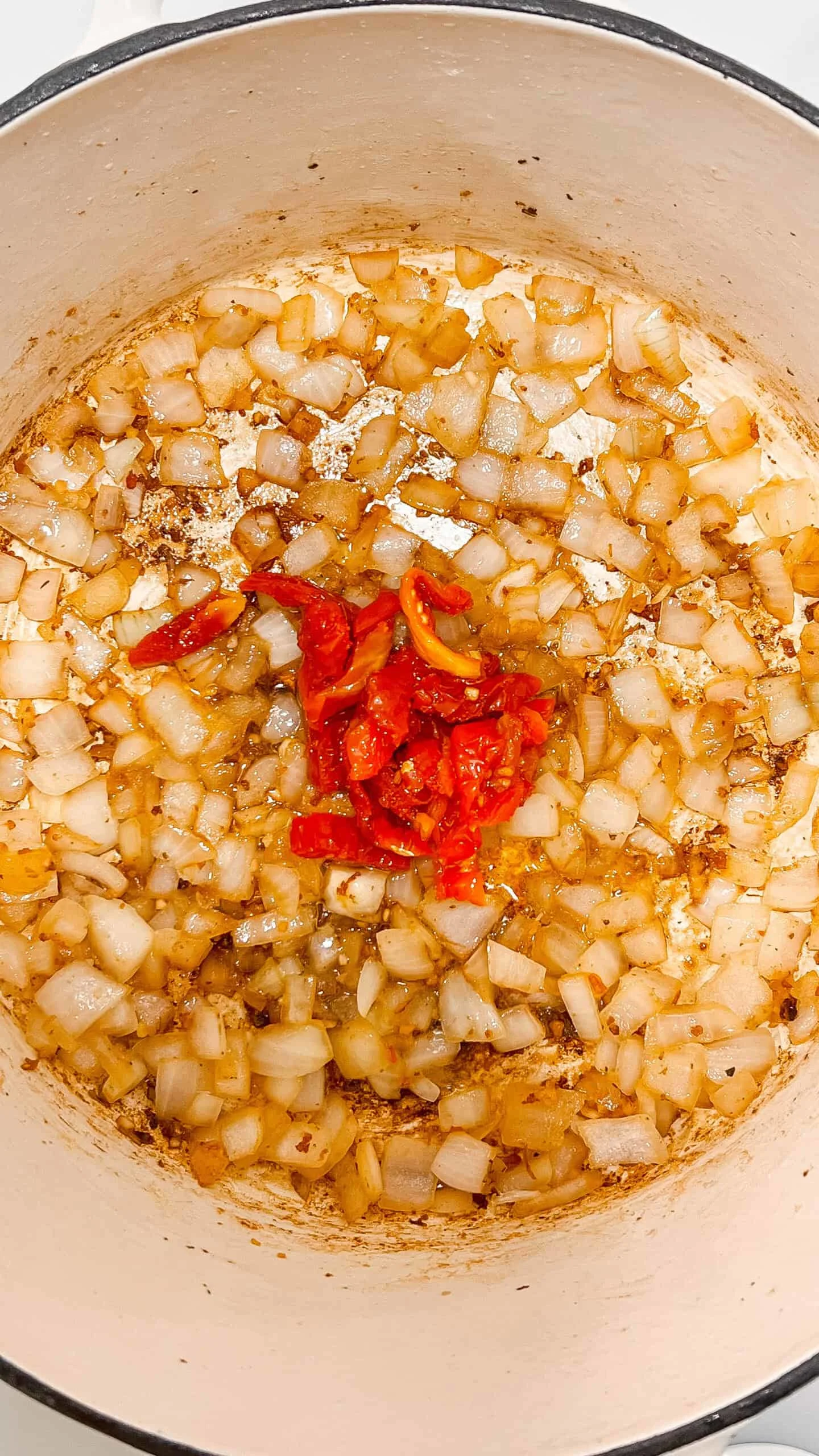 Saut&eacute;ed onions and red peppers in a cooking pot, perfect for flavorful dishes.