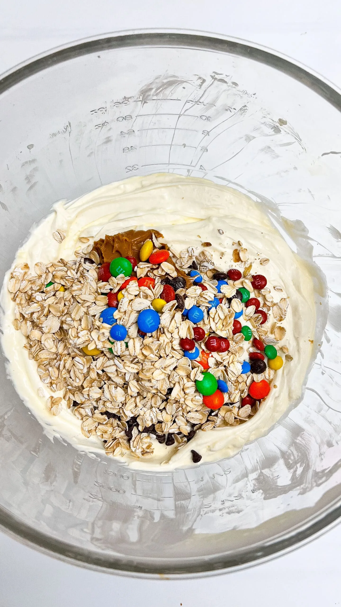 Creamy cheesecake batter with colorful M&Ms and oats in a transparent mixing bowl.