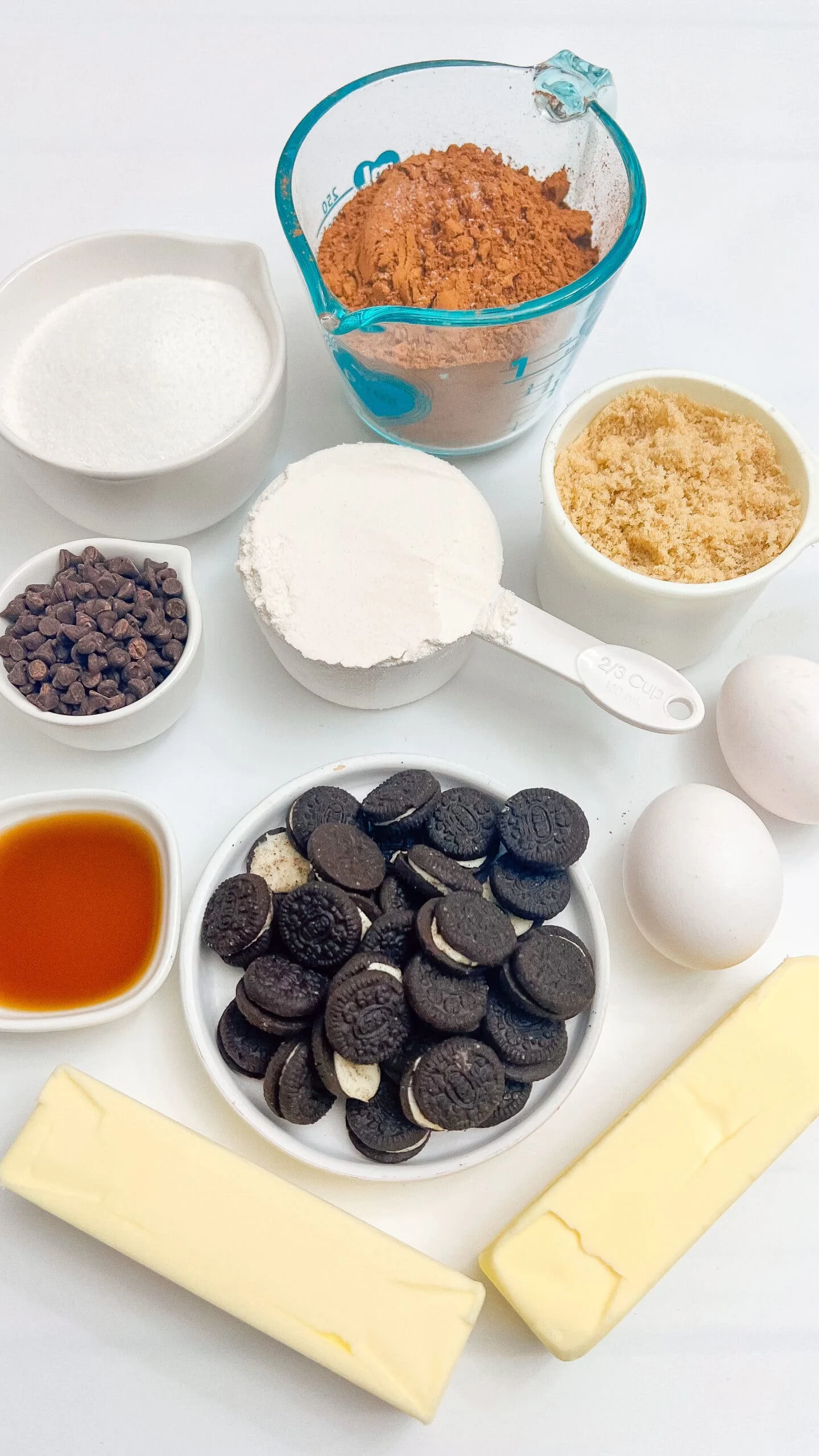 Rich ingredients for homemade chocolate cookies on a white surface, including Oreos, butter, eggs, and baking supplies.