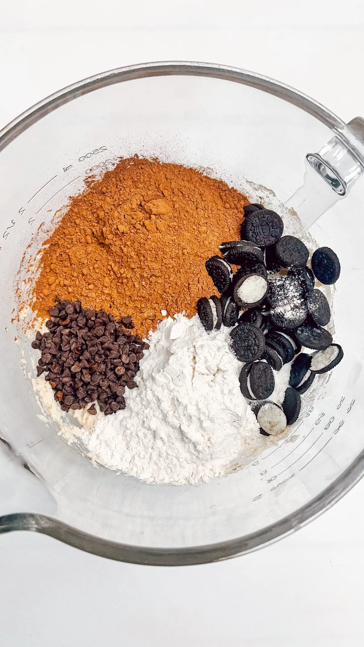 Delicious brownies ingredients including Oreos, chocolate chips, powdered sugar, and spices in a measuring cup.