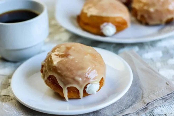 cream filled doughnut on white plate, doughnut in background cup of coffee