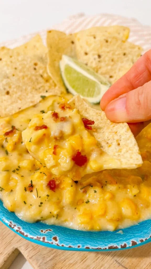 chip serving dipped corn dip Creamy crockpot corn dip recipe with cheese, bacon, and spices, ideal for parties and gatherings. Serve with tortilla chips.