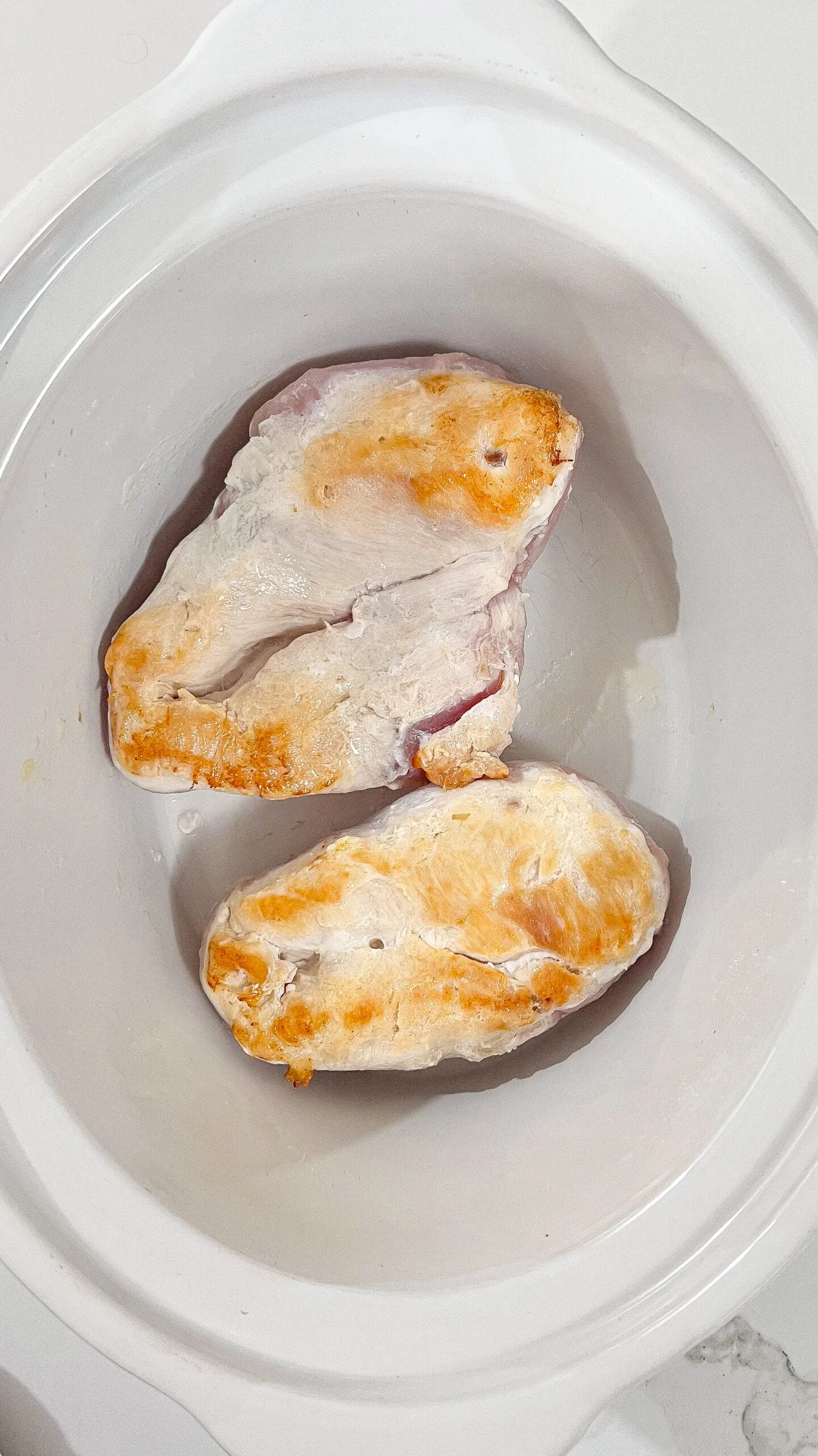 Raw chicken breasts in a Crockpot for Angel Chicken with garlic sauce.