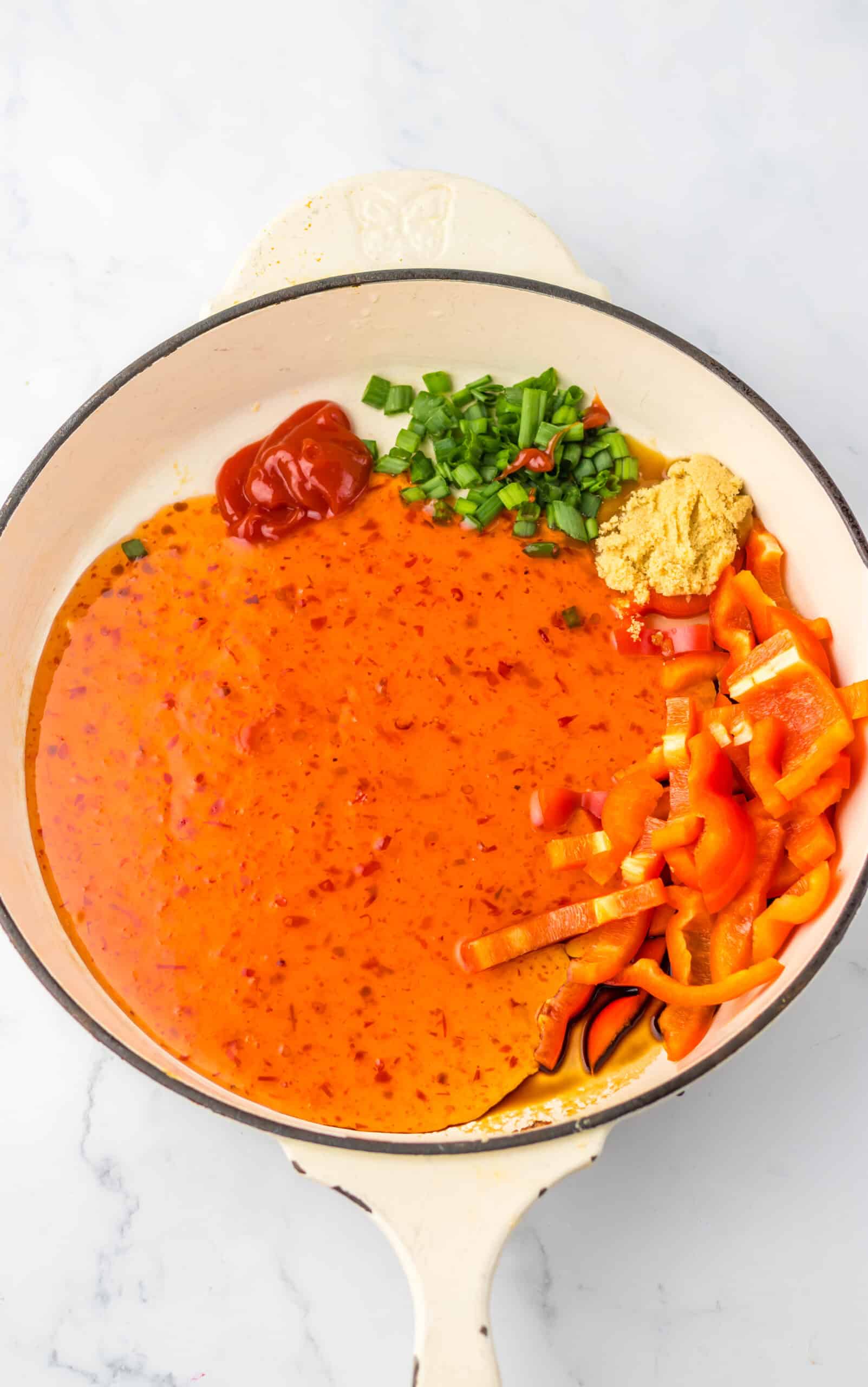 Sweet chili chicken sauce with chopped green onions, ginger, and red pepper flakes in a bowl.