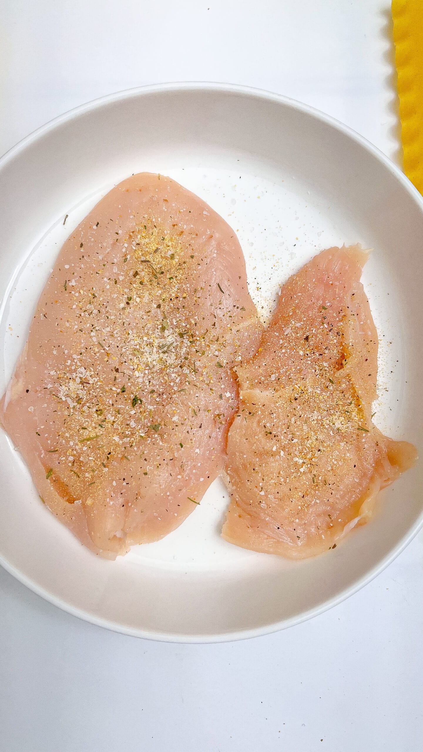 Raw chicken breasts seasoned with pepper in a white bowl.