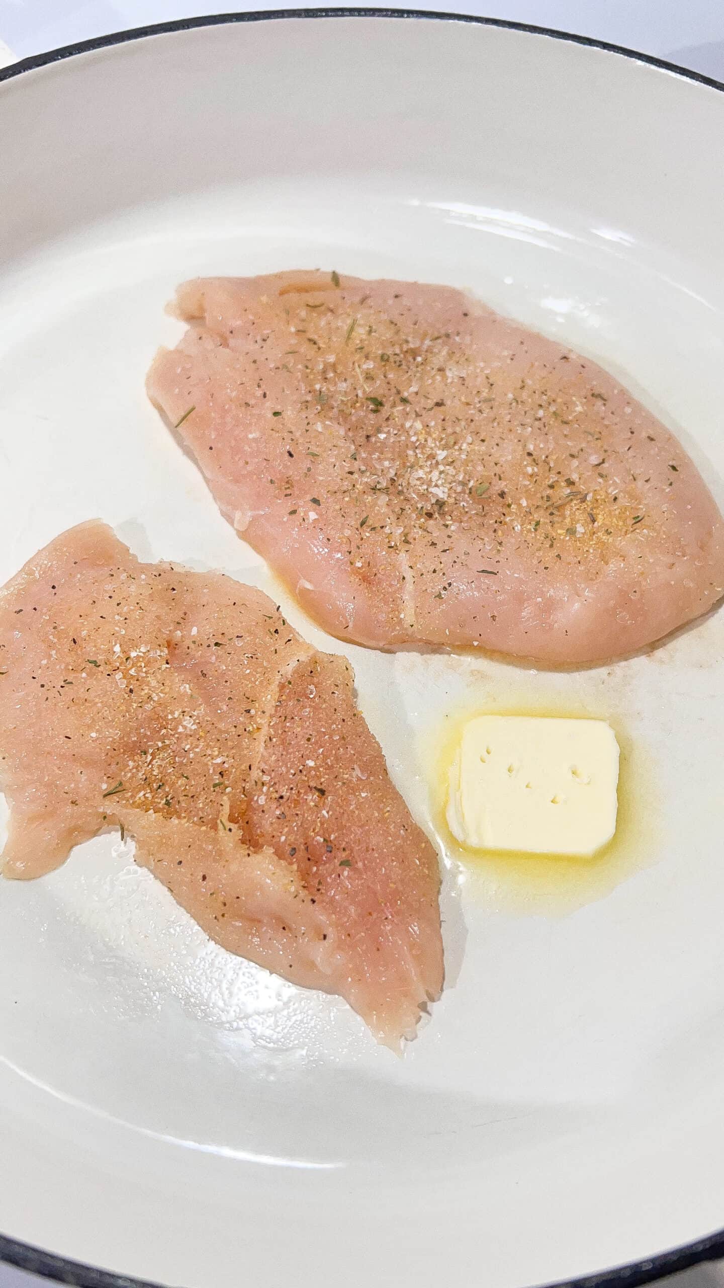 Raw chicken breasts seasoned with salt and pepper in a skillet.