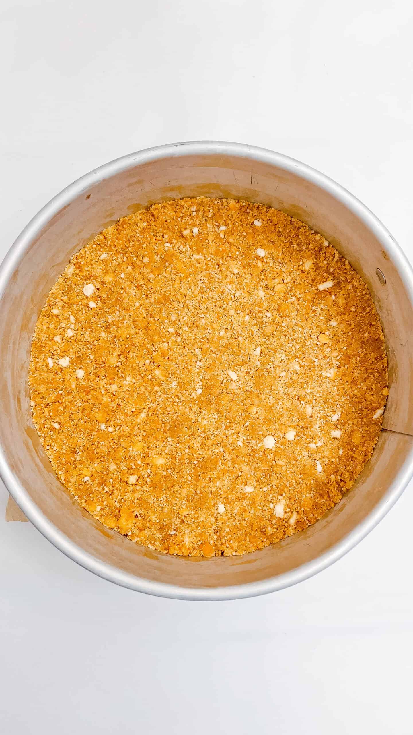 Close-up of crumbly Muddy Buddy cheesecake crust in a round pan.