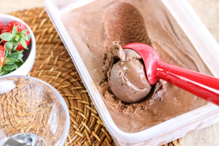 Creamy chocolate ice cream in a plastic container with a red scoop. Perfect treat for hot days or de.