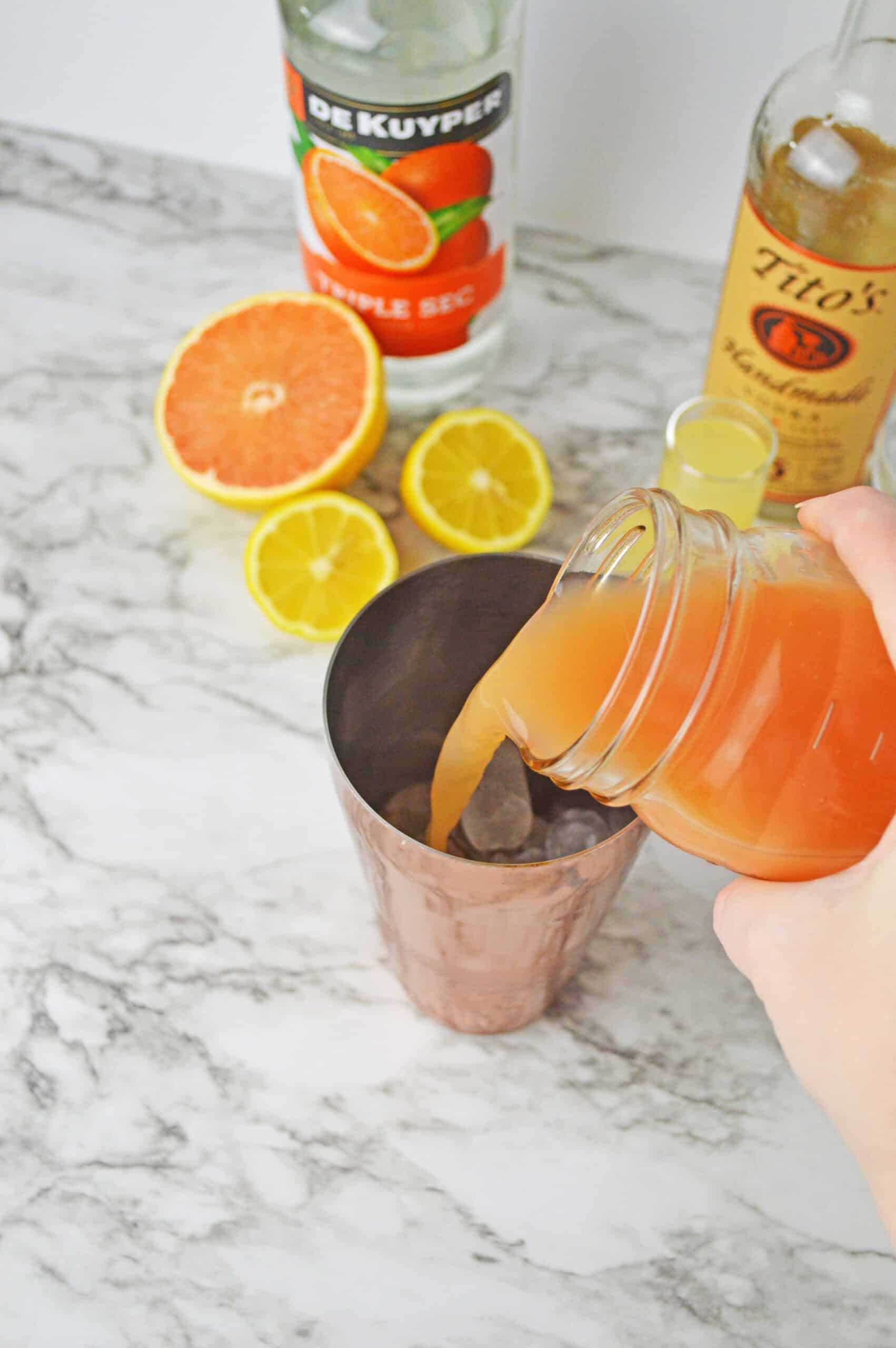 Pouring grapefruit juice into a cocktail shaker for a refreshing grapefruit martini.